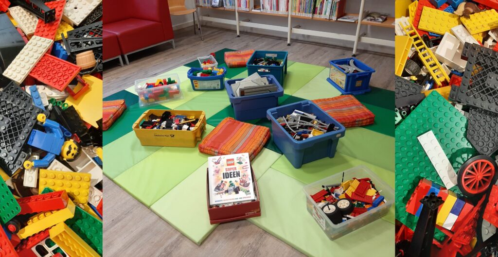 Auf dem Boden der Kinderbücherei stehen Kisten gefüllt mit Lego-Bausteinen.